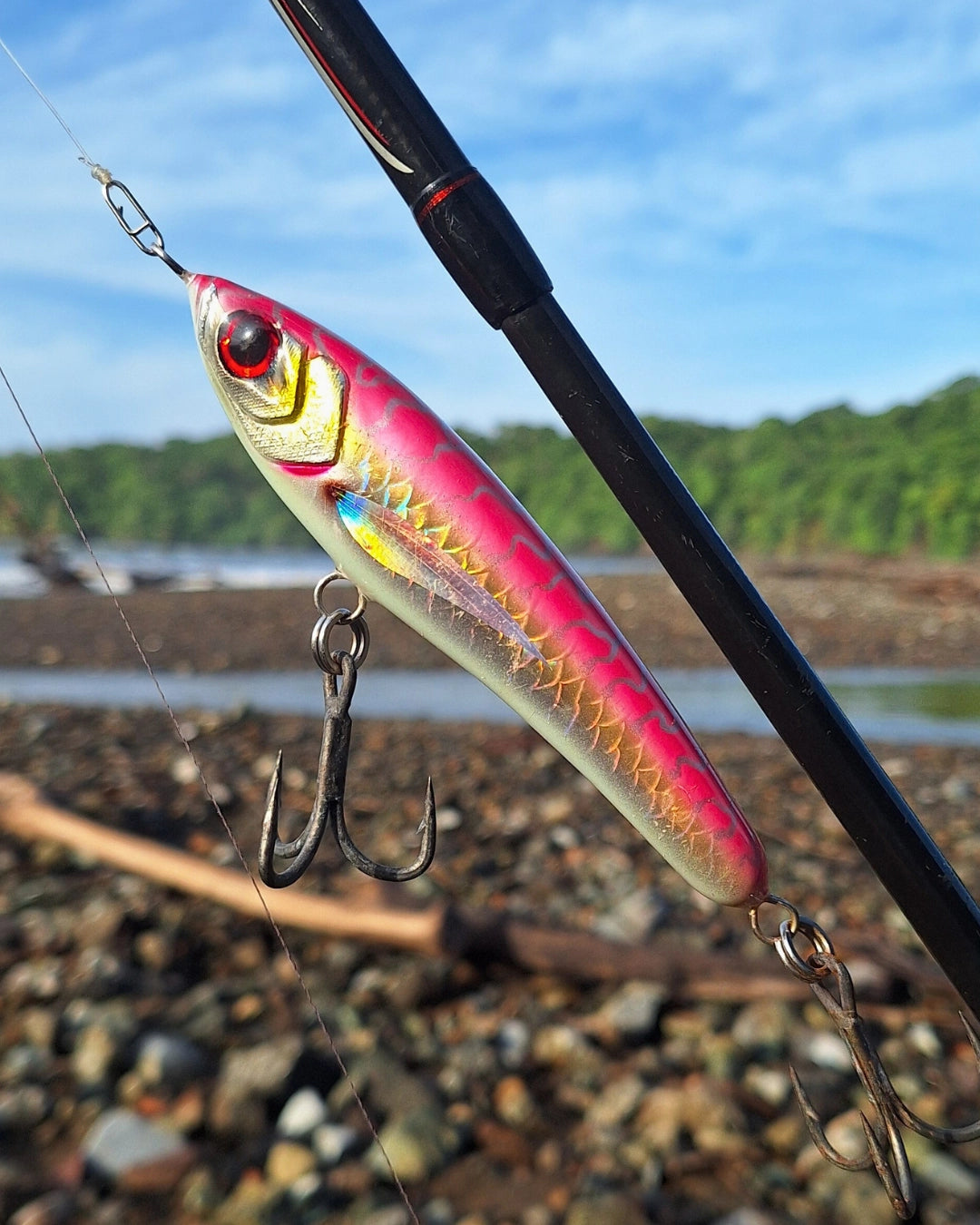 Pink  and white timber fishing lure with holographic scales on a fishing rod.