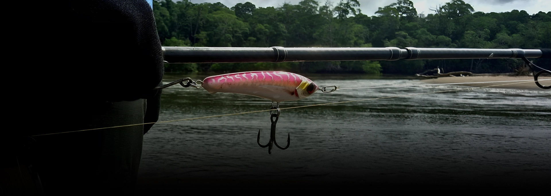 Pink, silver and white timber fishing lure with river estury in the background.